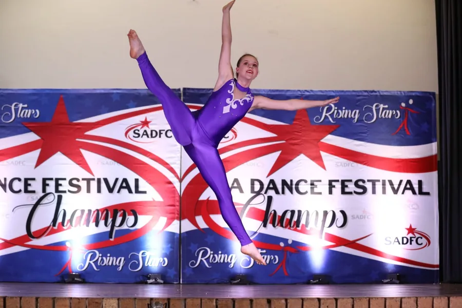 Thalia mid-leap on stage, legs split in the air and both arms extended