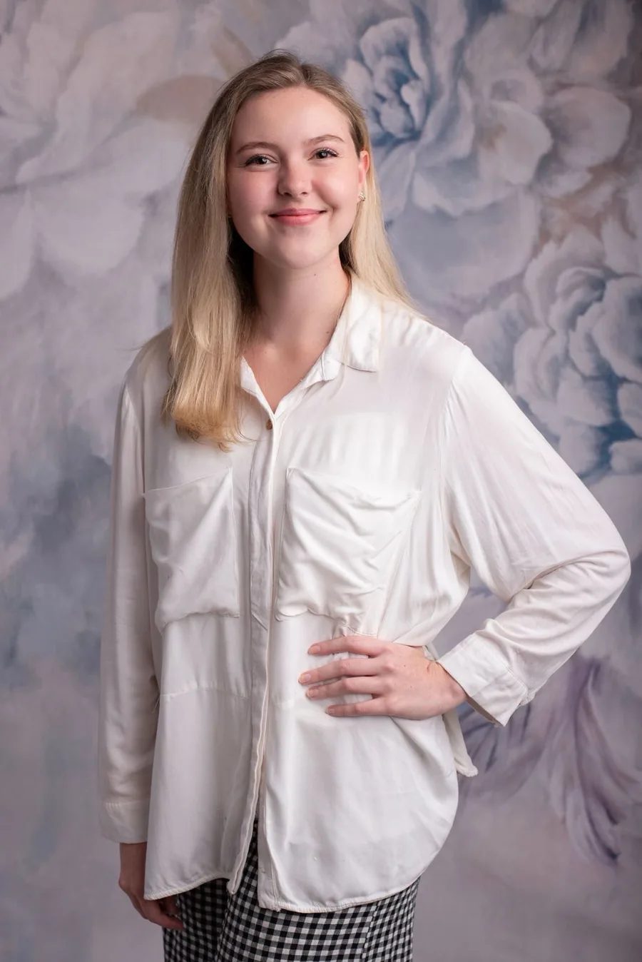 Thalia standing in a white shirt, smiling in front of a painted floral backdrop
